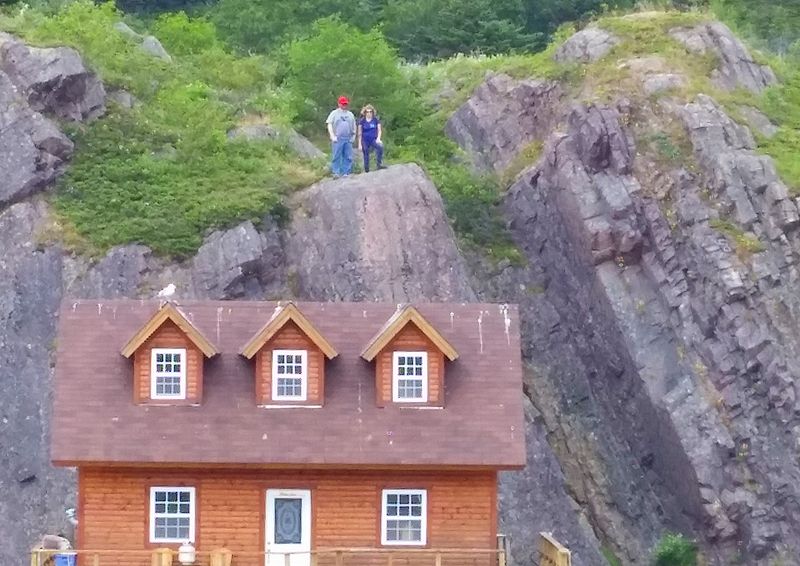 People stand on a cliff above a house